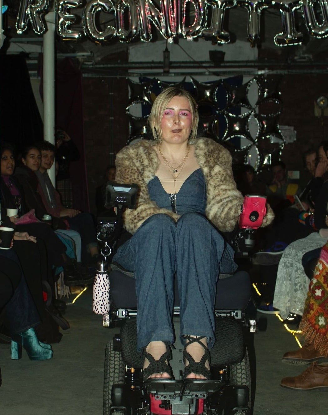 Rae, a wheelchair user in a denim jumpsuit and fur bolero.