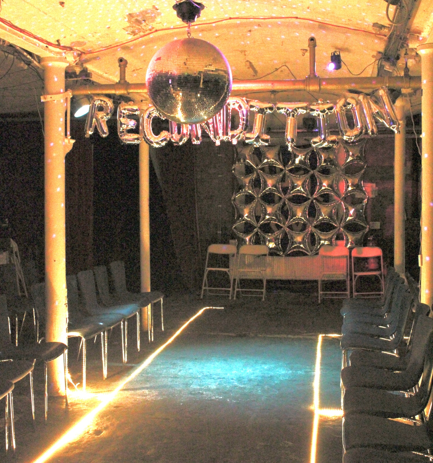 ID: Image of the Recondition catwalk decorated with silver balloons and warm lights
